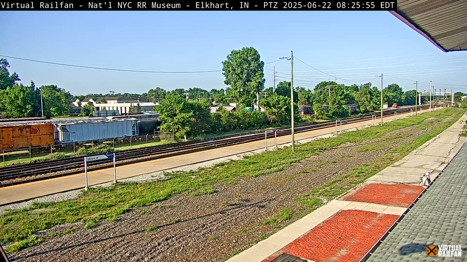A long train track with several freight cars and a few buildings in the distance under a clear sky.