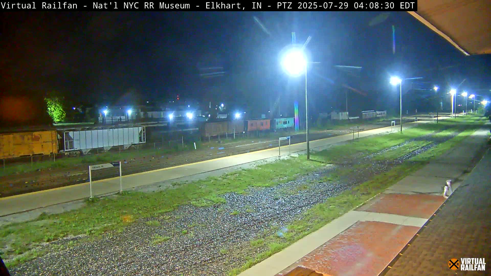 A nighttime view of a railroad platform with several train cars parked nearby, under bright artificial lights.