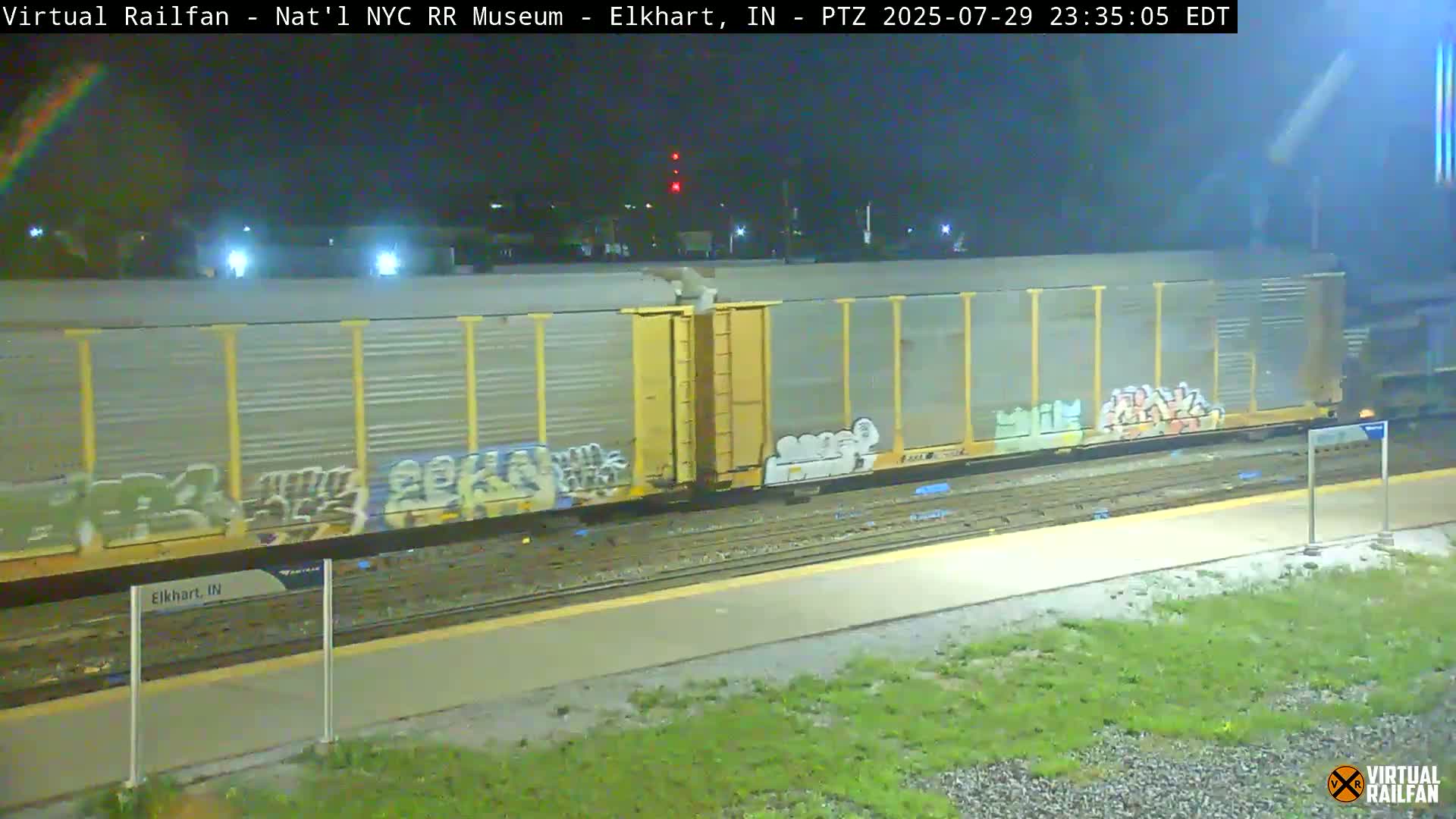 A nighttime view of a railroad platform with several train cars parked nearby, under bright artificial lights.