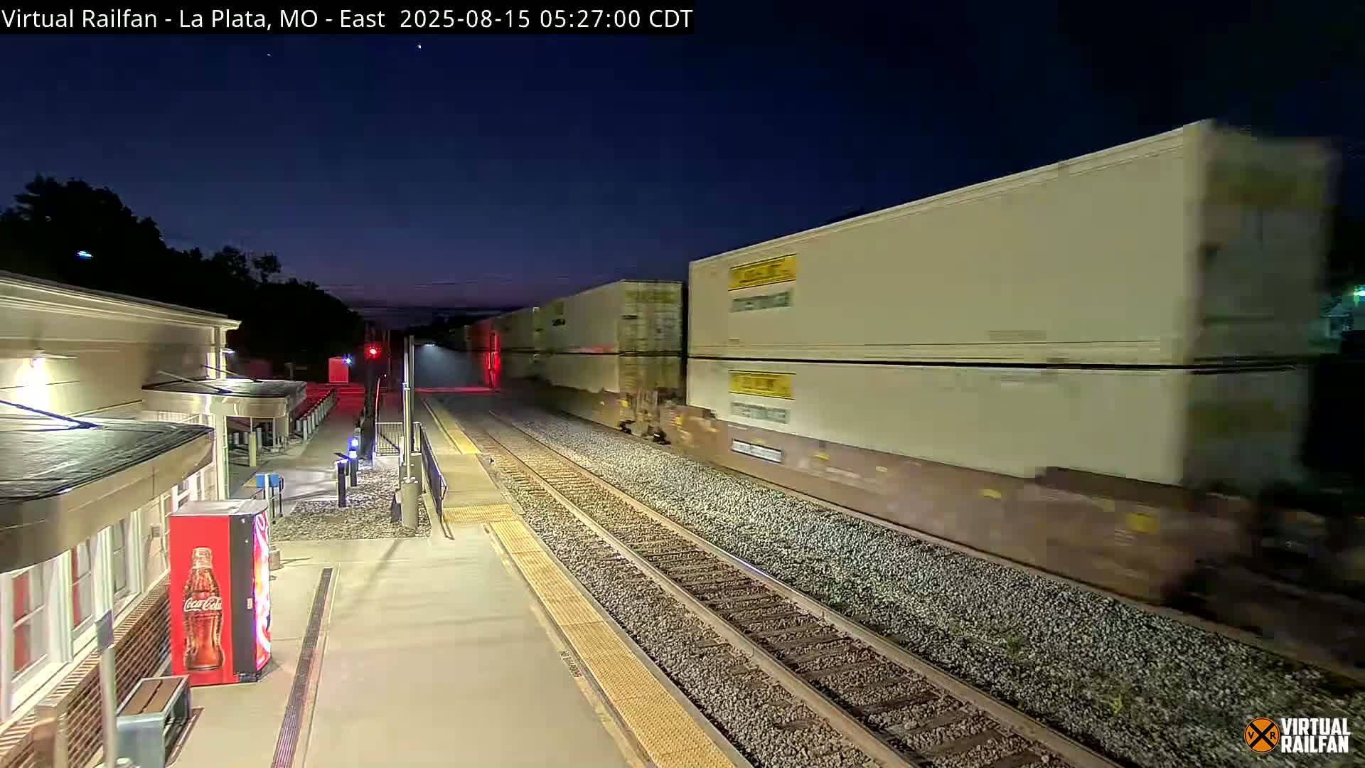 A nighttime view of a railroad platform with several train cars parked nearby, under bright artificial lights.