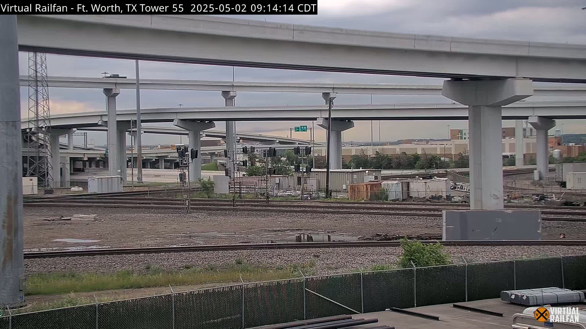 A view of a railway yard under a large overpass system on an overcast day.