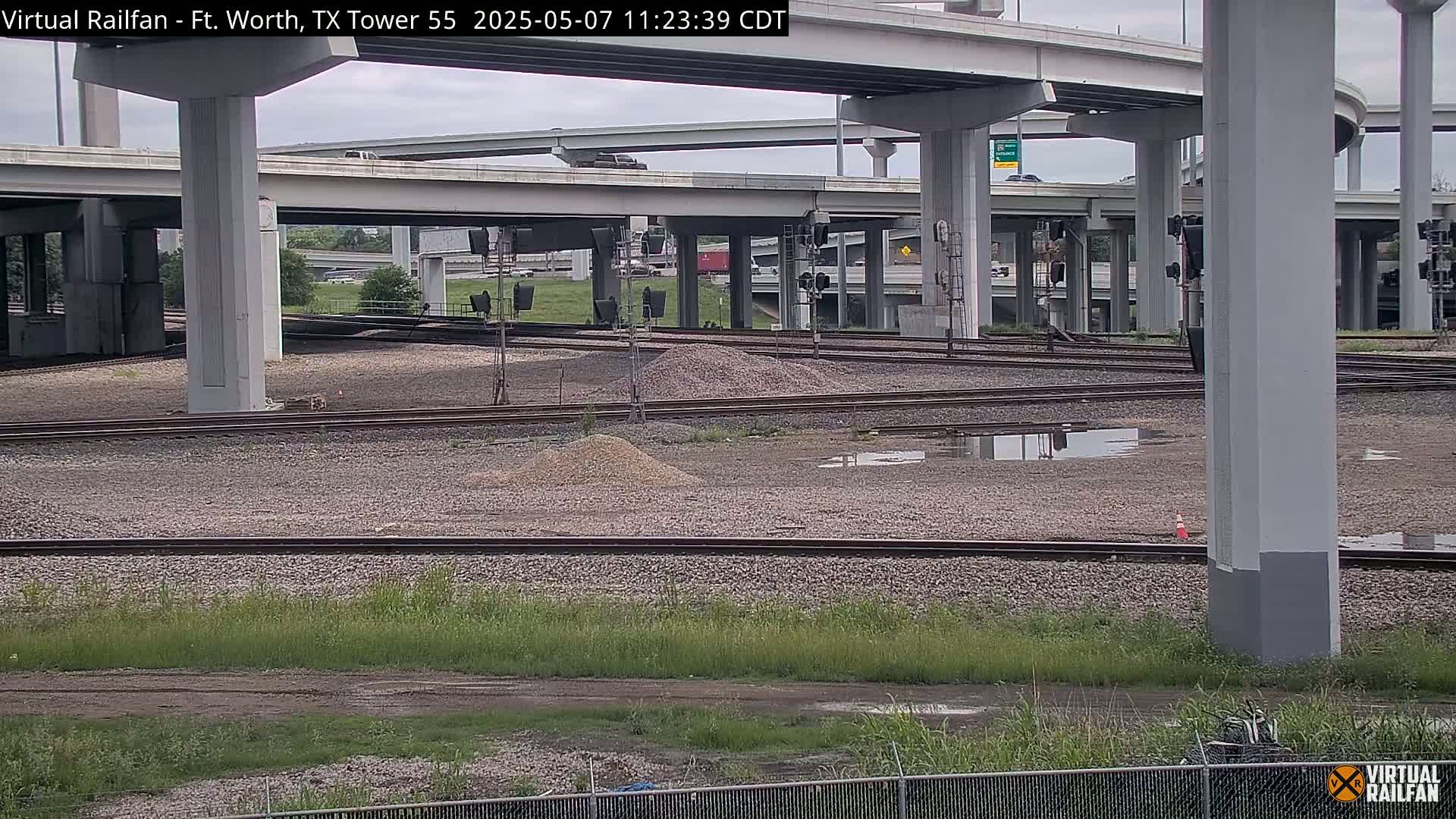 A view of railroad tracks and an overpass under a partly cloudy sky.