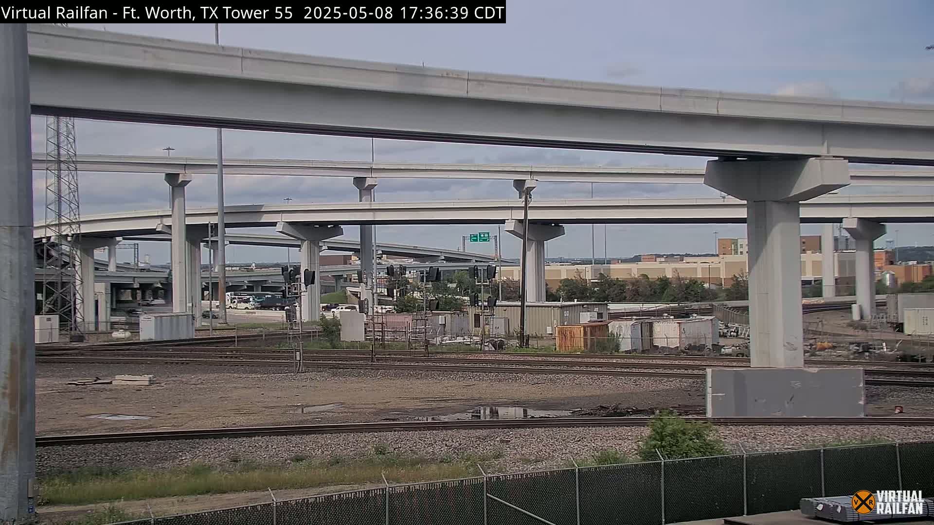 A view of railroad tracks and an extensive highway overpass system under a partly cloudy sky.