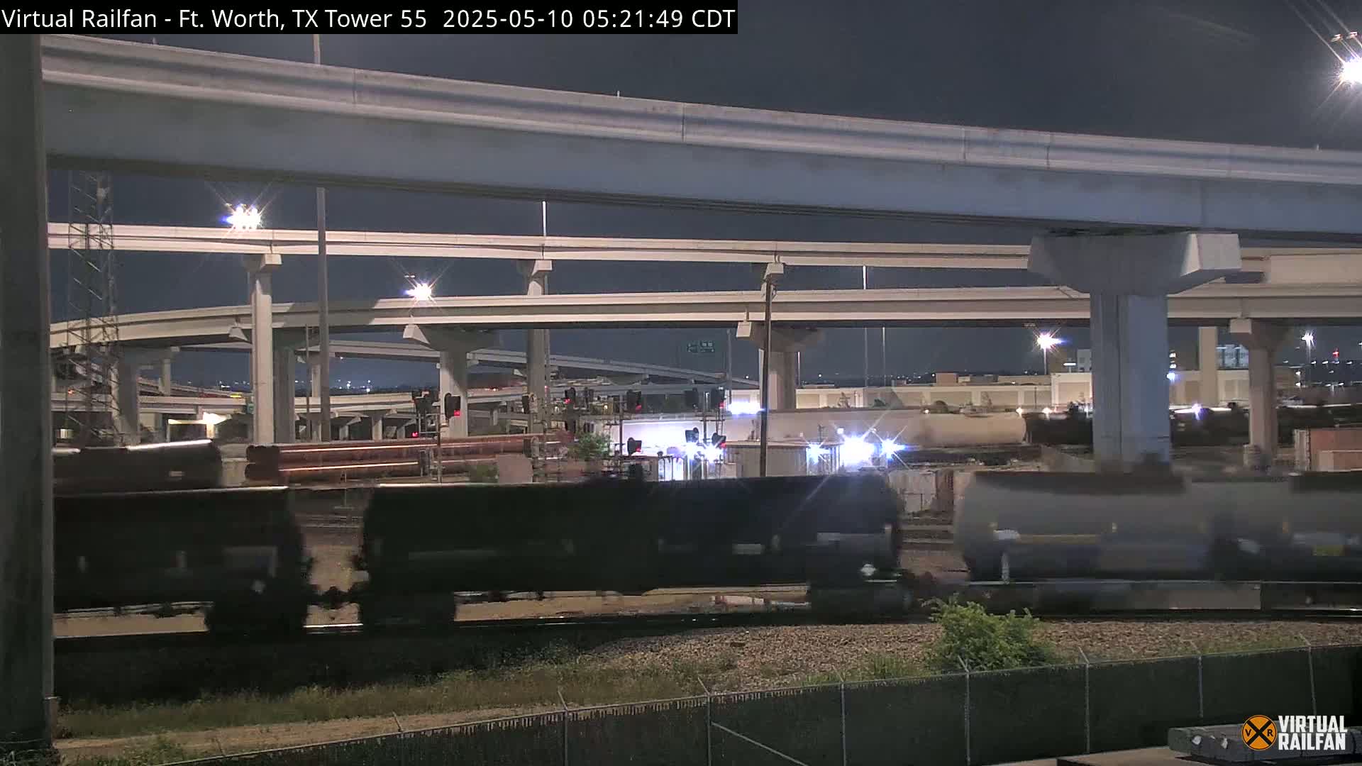 A freight train moves through a complex highway interchange at night.