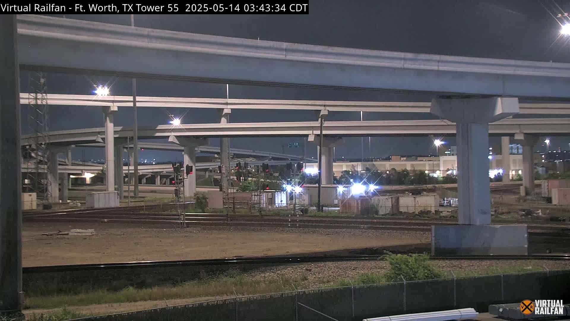 At night, under a dark sky, a complex system of elevated highways and railway tracks intersect.
