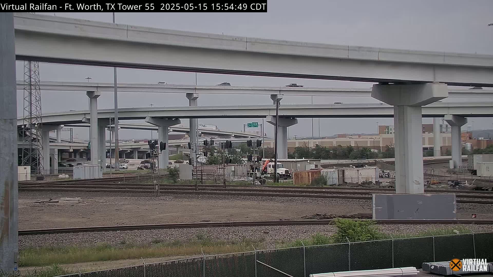 A view of a large highway interchange under a cloudy sky, with railroad tracks and construction equipment visible in the foreground.