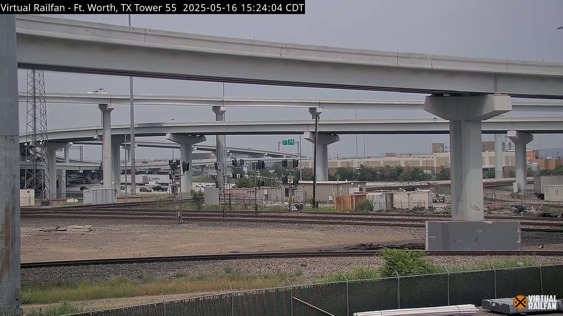 An overcast sky hangs over a railroad crossing beneath a complex highway overpass.