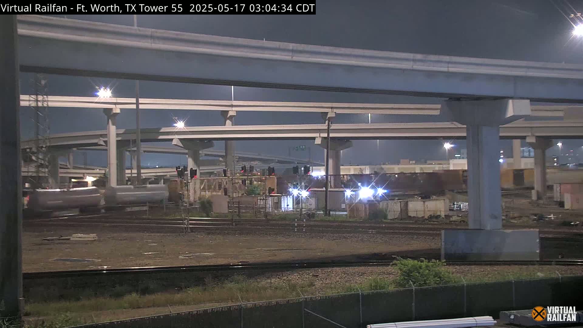 At night, a train passes under a large highway overpass.