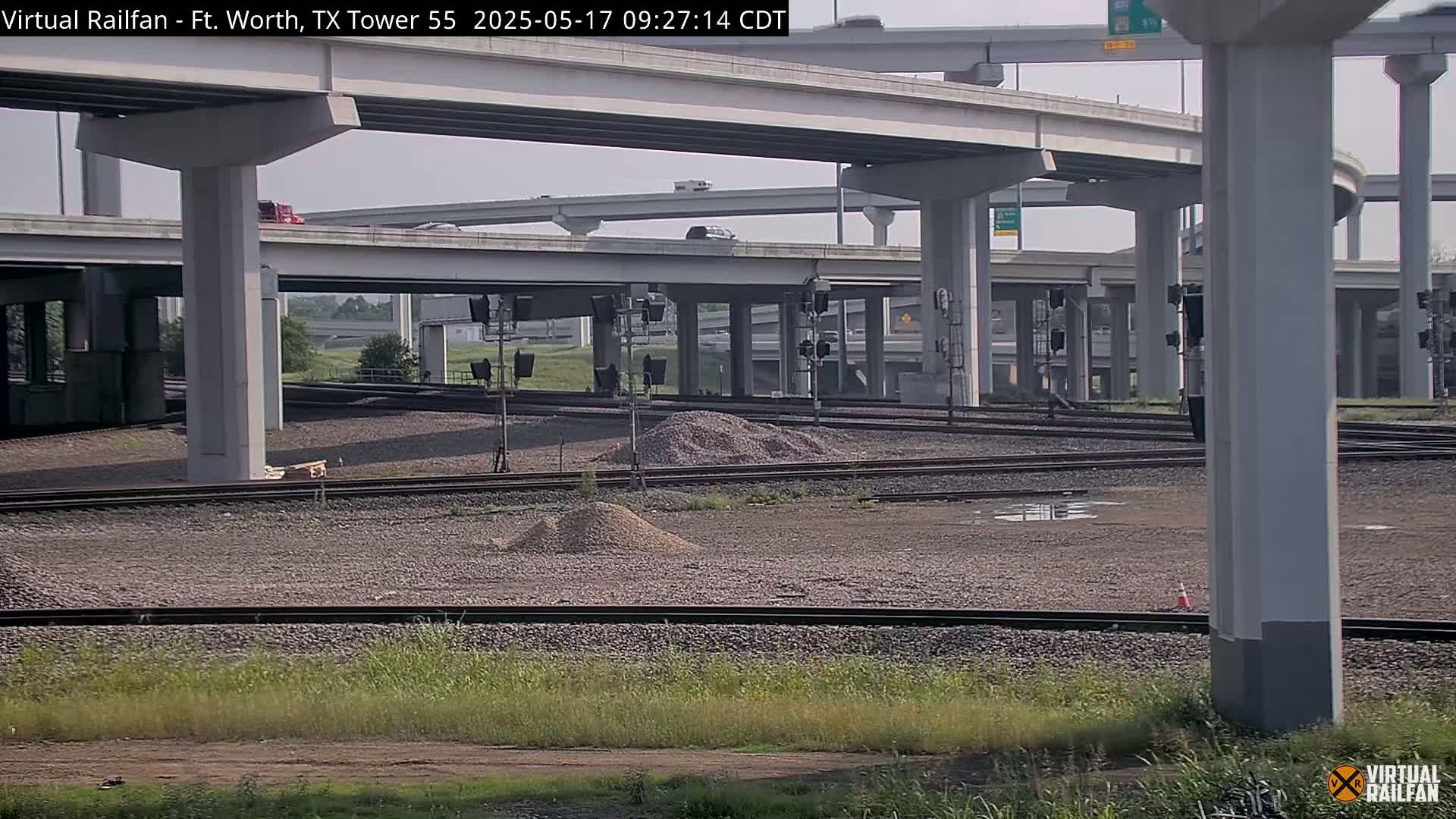 A view of railroad tracks and a highway overpass on a partly sunny day.