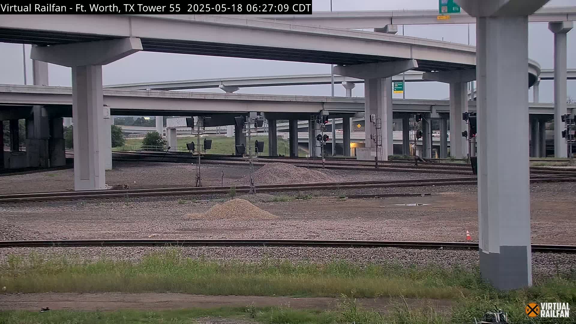A section of railway tracks lies beneath a complex overpass system on an overcast day.
