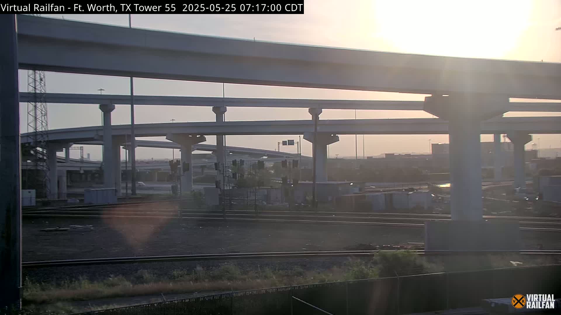 A hazy sunrise illuminates a complex highway interchange and nearby train tracks.