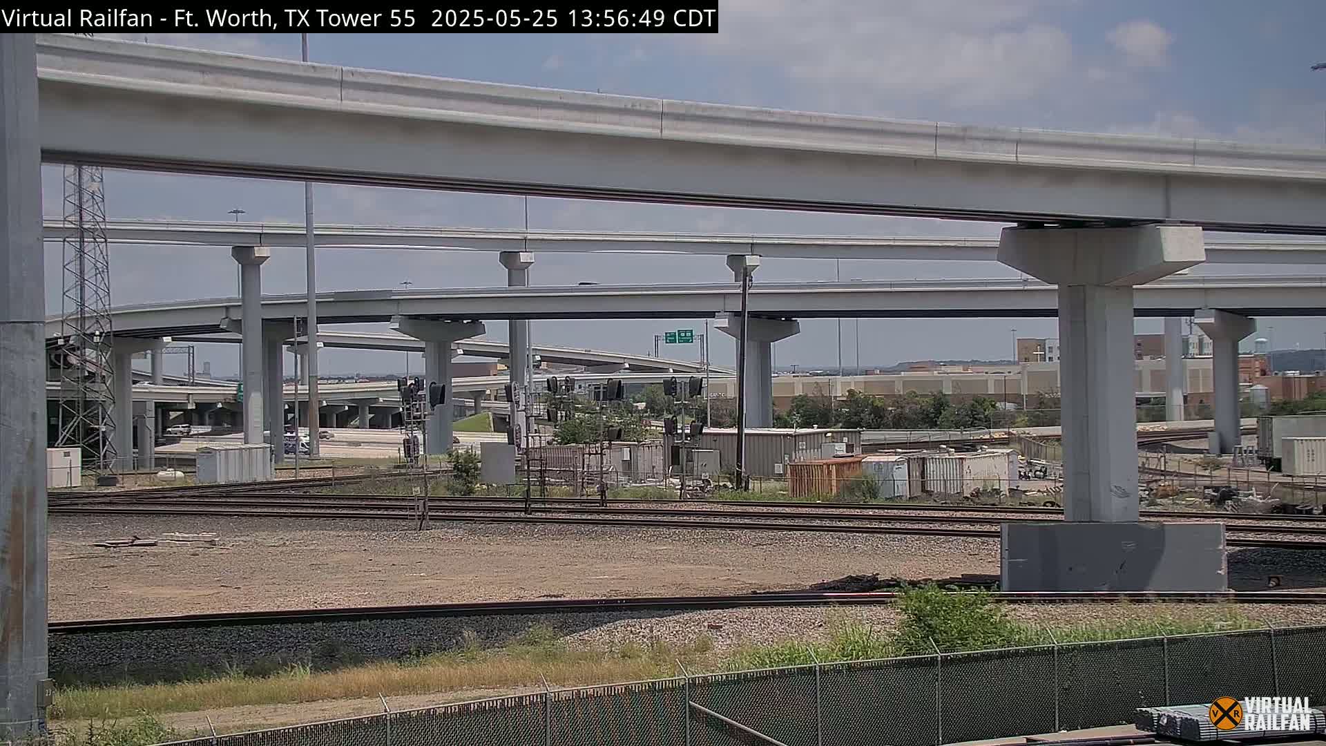 A view of a large highway overpass and railroad tracks beneath it on a partly sunny day.