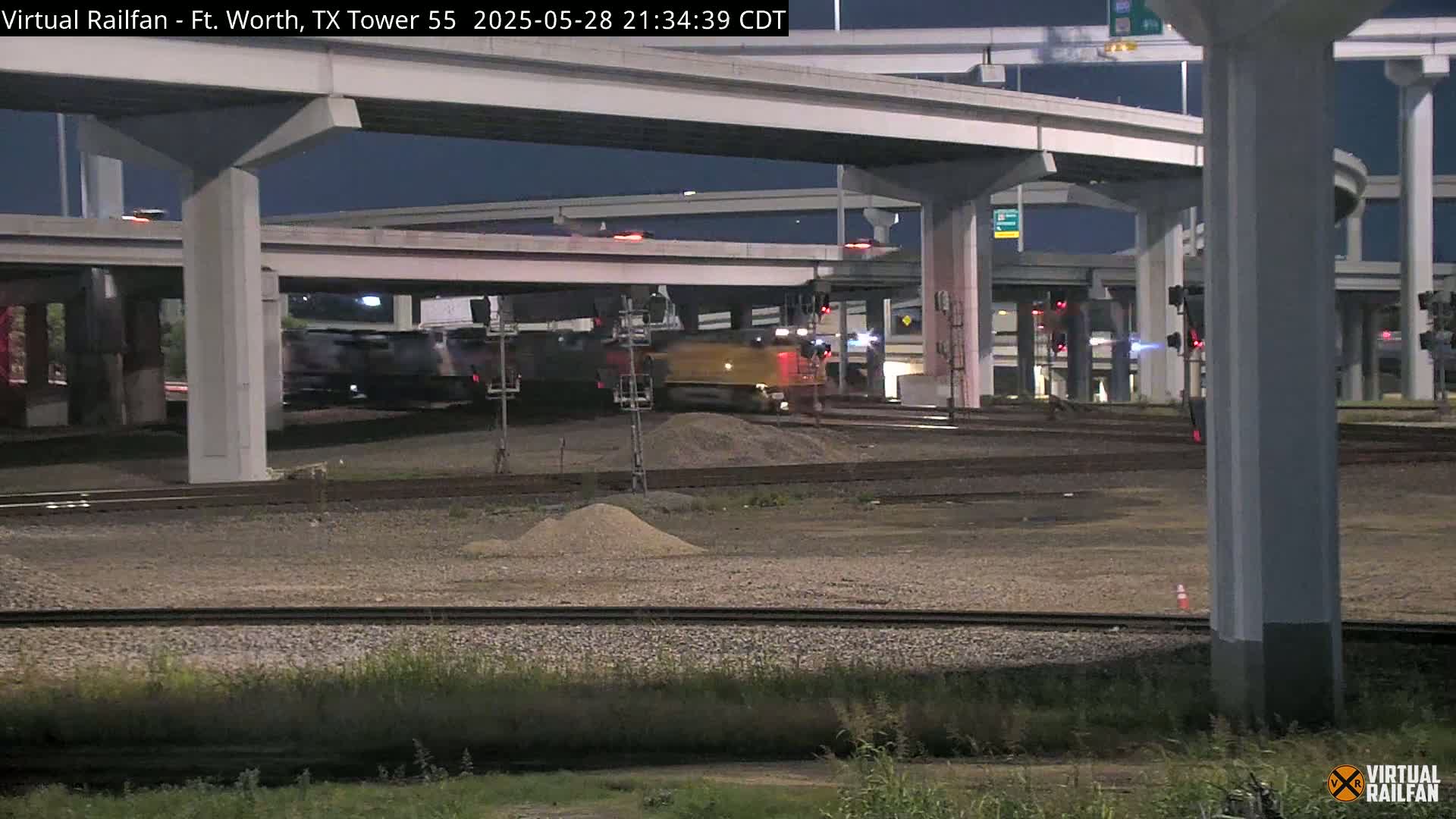 A freight train passes under an overpass at night.