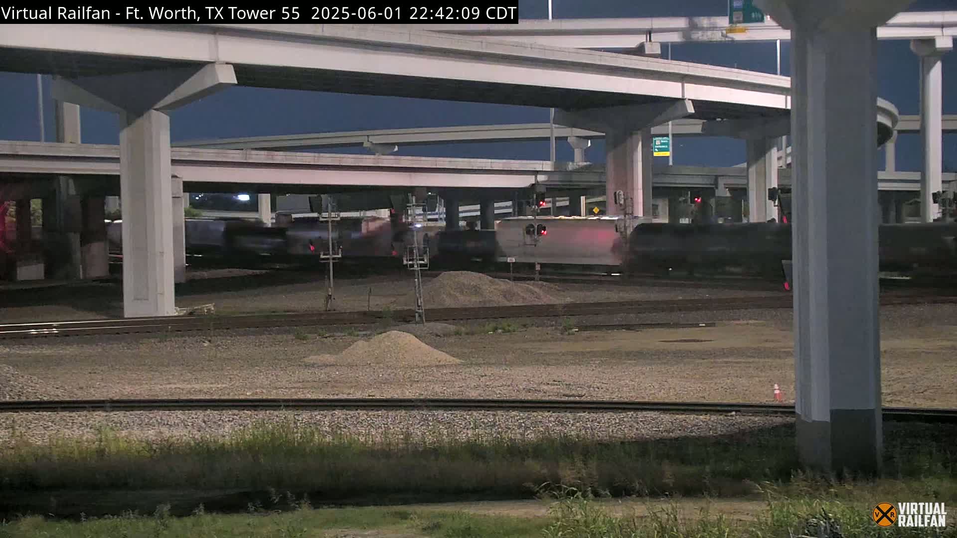 A freight train passes under an overpass at night.