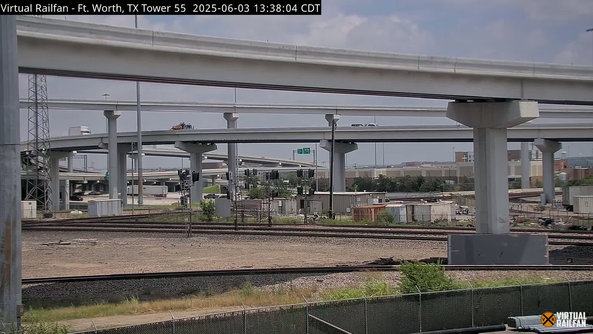 A view of an elevated highway interchange over railroad tracks on a partly cloudy day.