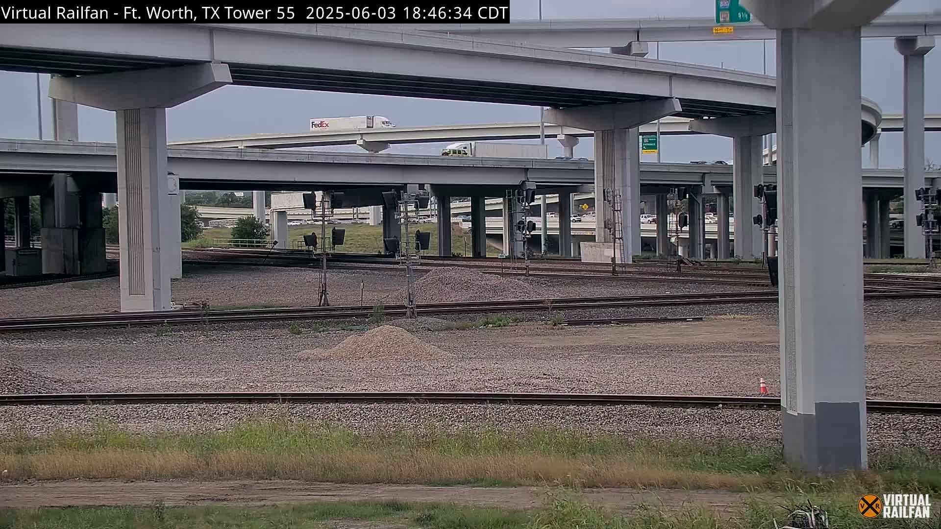 A view of railroad tracks and a highway overpass under a partly cloudy sky.
