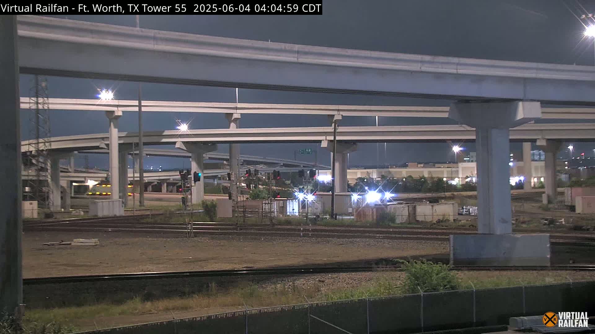 A nighttime view of a complex highway interchange over railroad tracks, under a dark sky.
