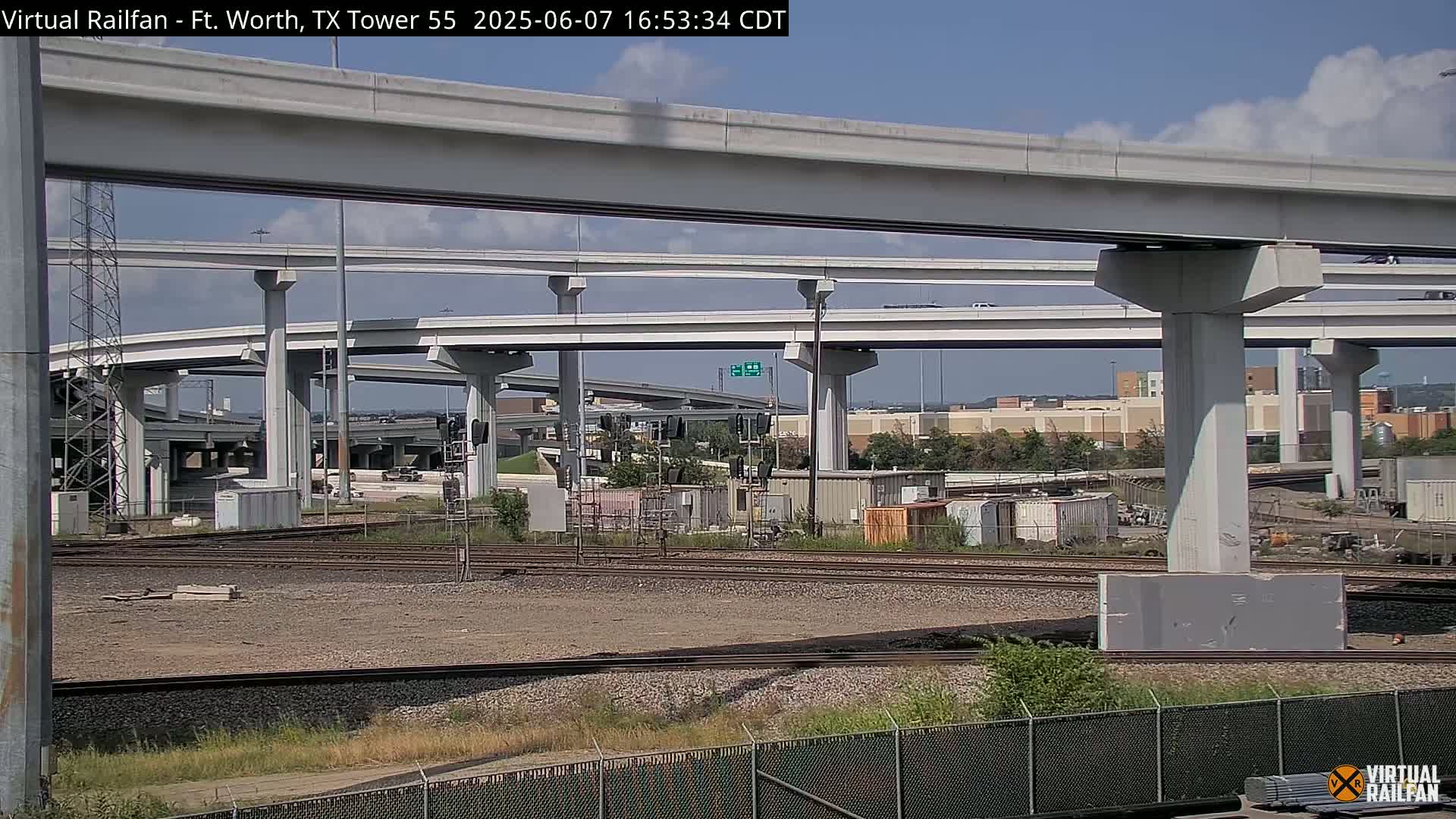 A view of a large highway overpass and railway tracks below, under a partly cloudy sky.