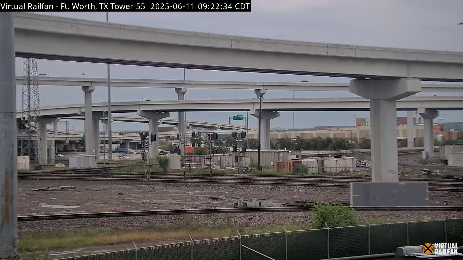 A view of an elevated highway overpass system and railroad tracks under an overcast sky.