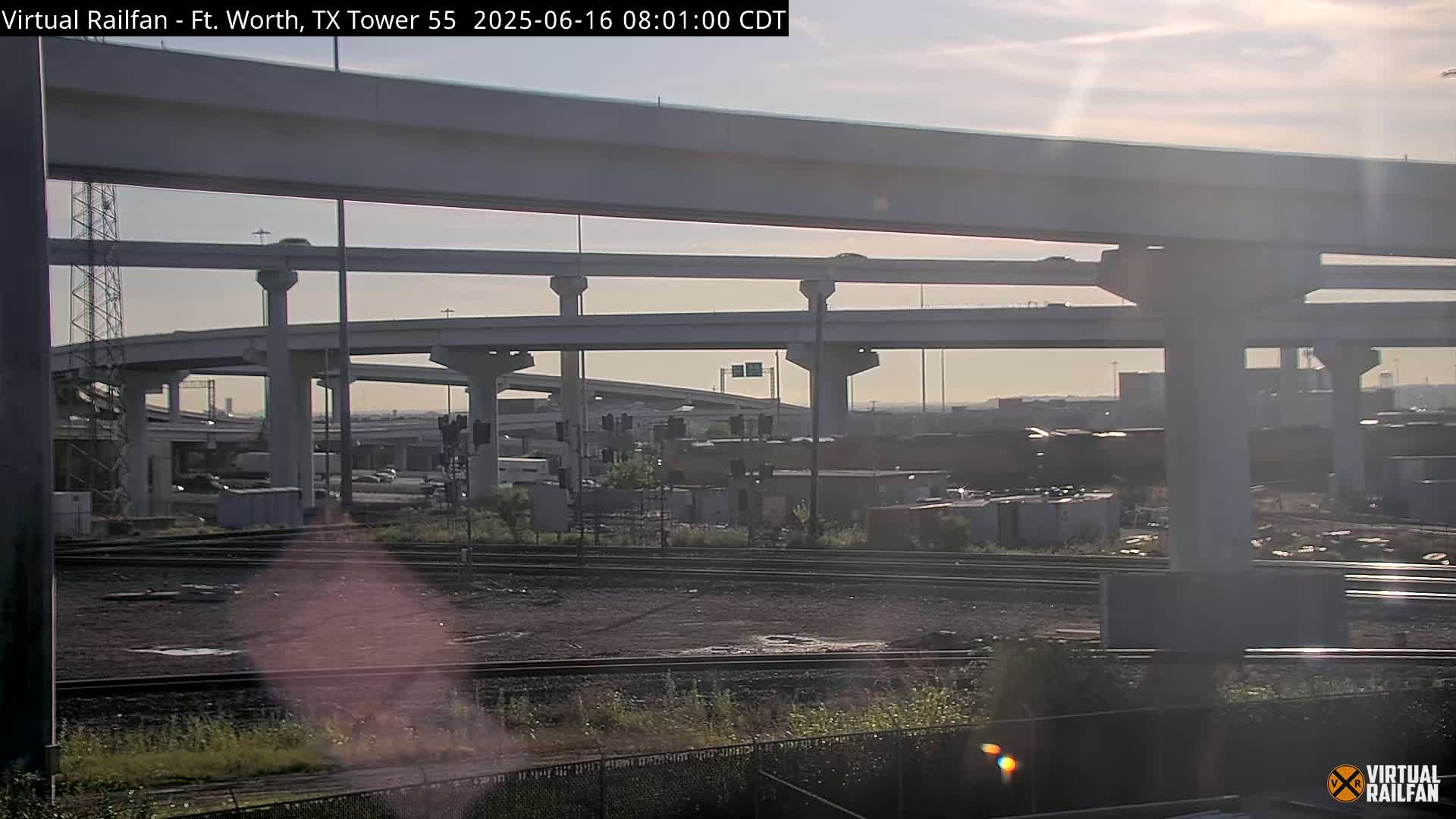 A view of a large highway interchange and railroad tracks below on a partly sunny day.