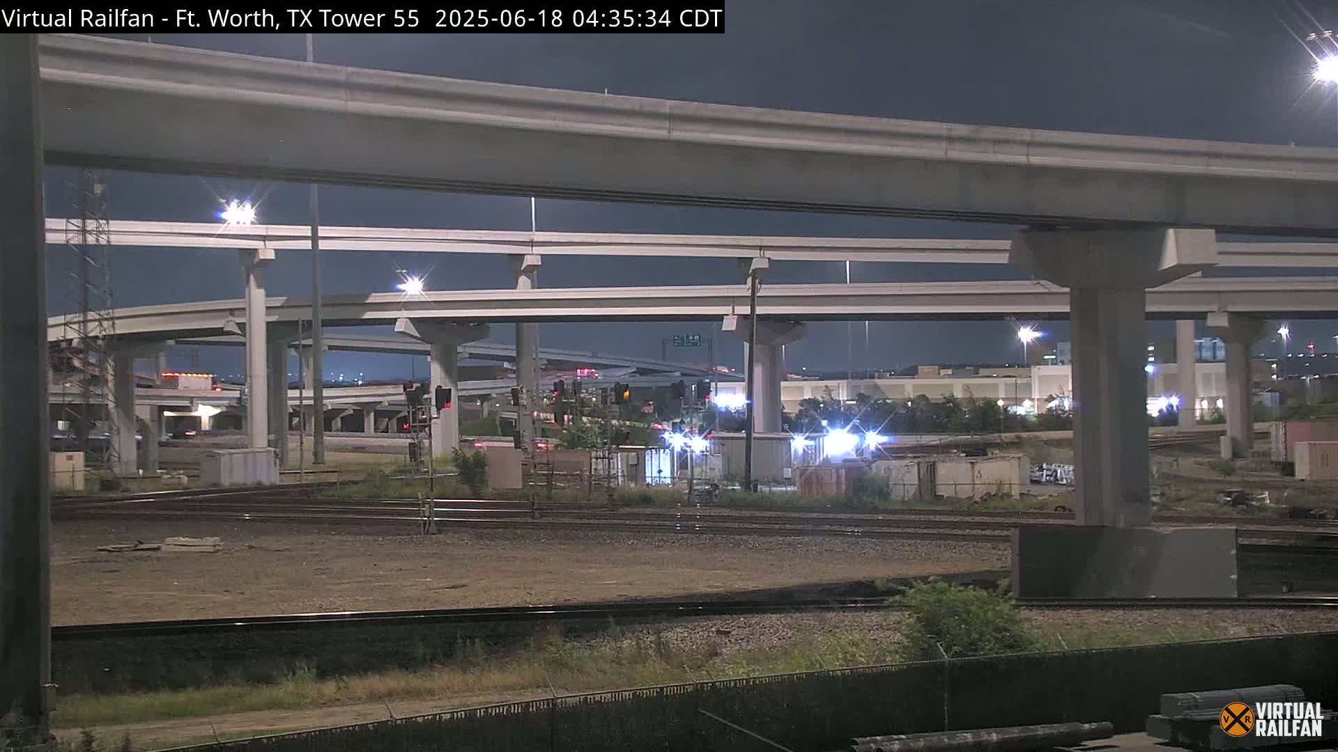 A nighttime view of an intricate highway overpass system intersecting with railroad tracks, under a dark sky.