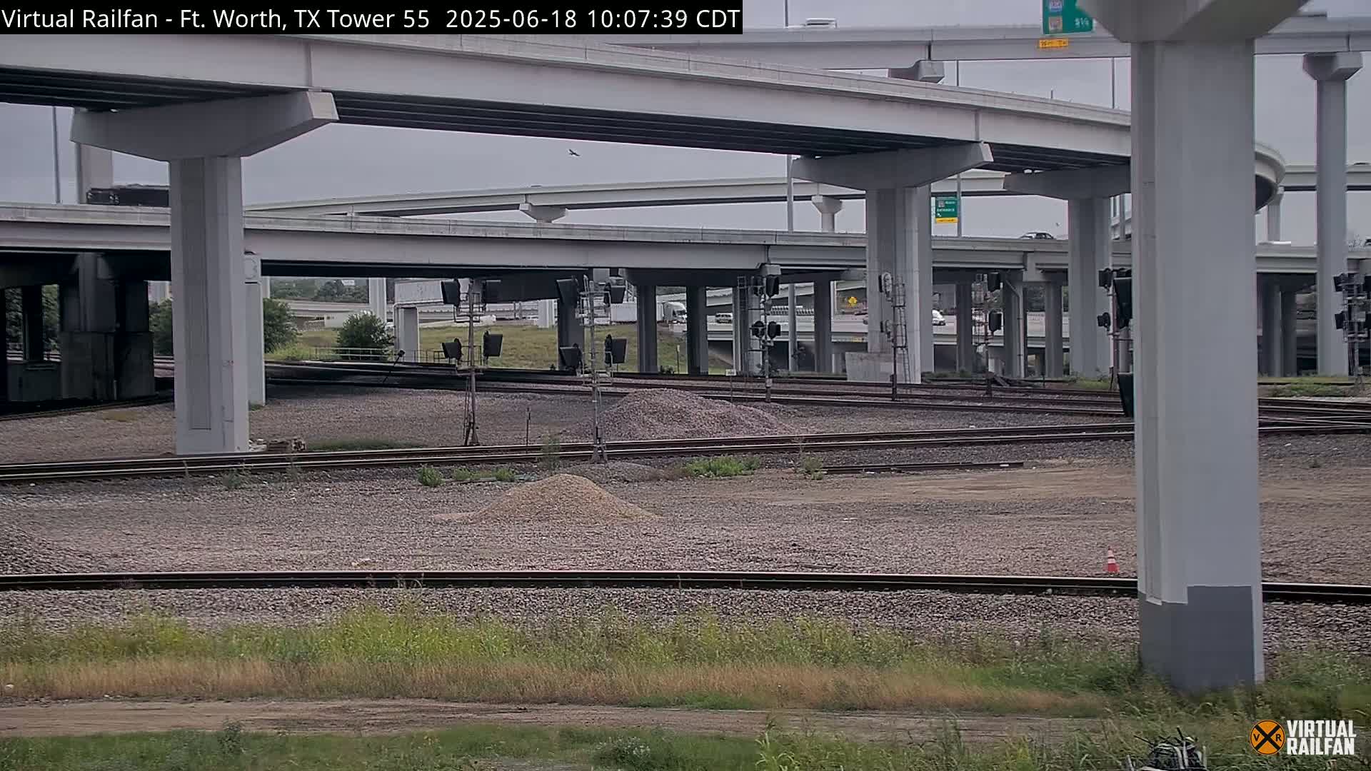 A section of railway tracks lies beneath a complex overpass system on an overcast day.
