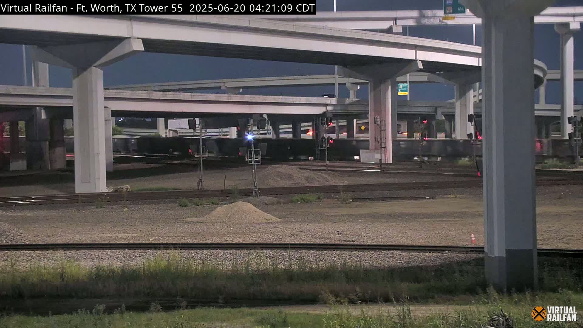 At night, a freight train passes under a complex highway overpass.