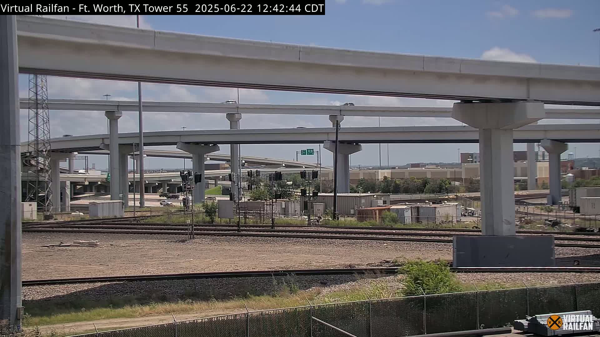 A view of a multi-level highway overpass and railroad tracks on a partly sunny day.
