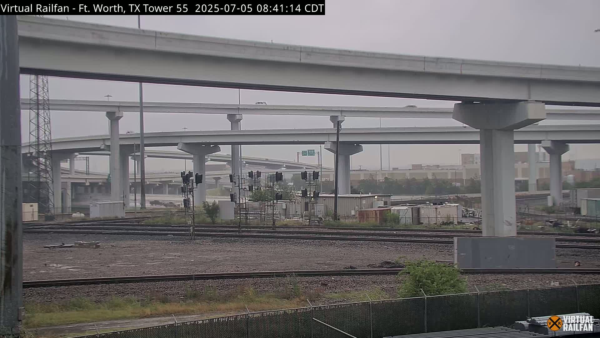 Overcast skies loom over a sprawling highway interchange and railroad tracks.