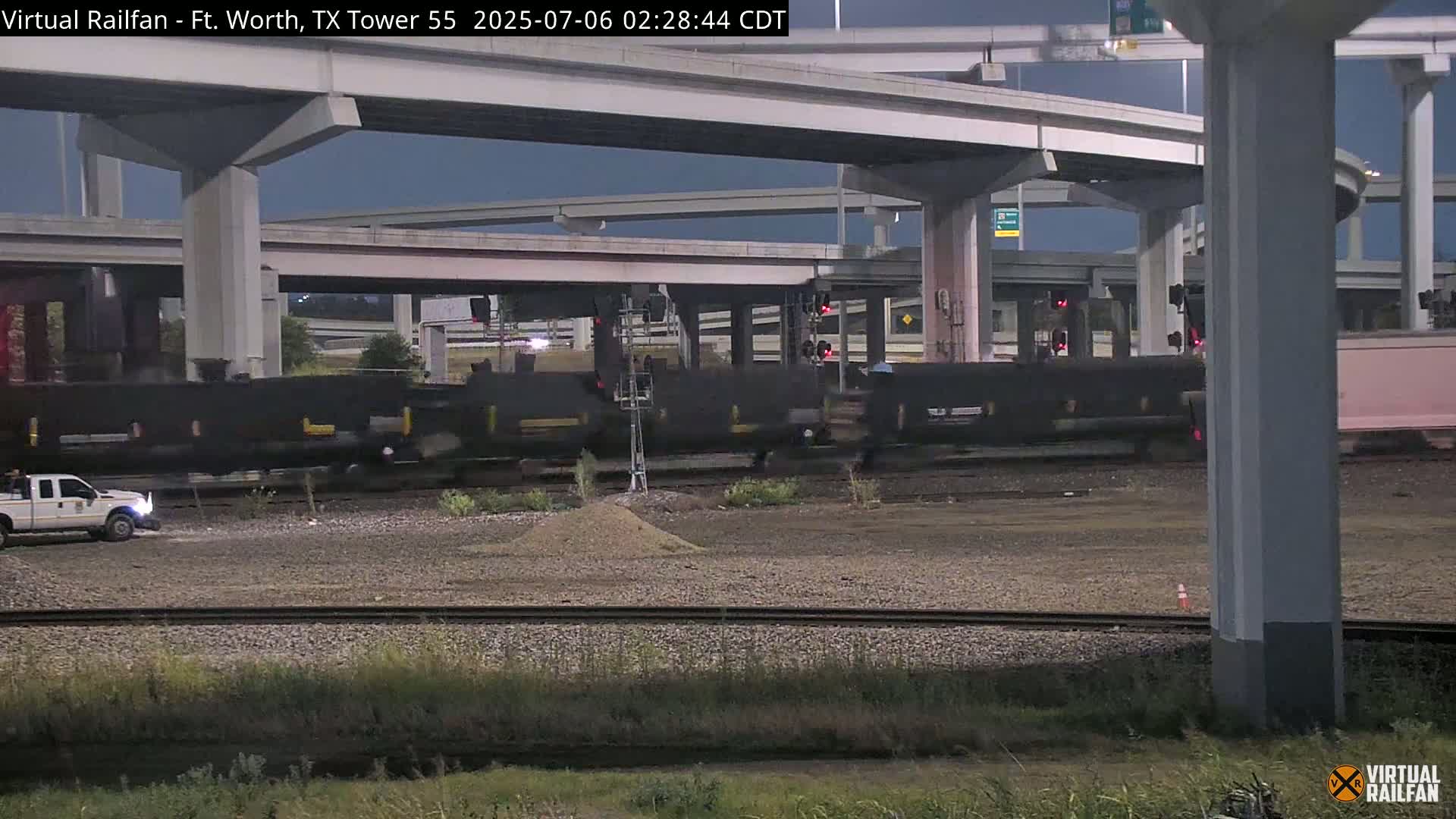 A long freight train passes under an elevated highway at night.