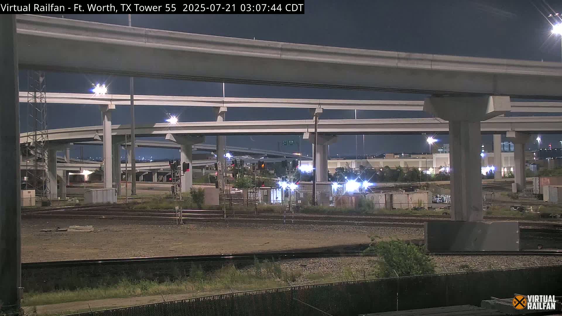 A nighttime view of a complex highway interchange over railroad tracks.