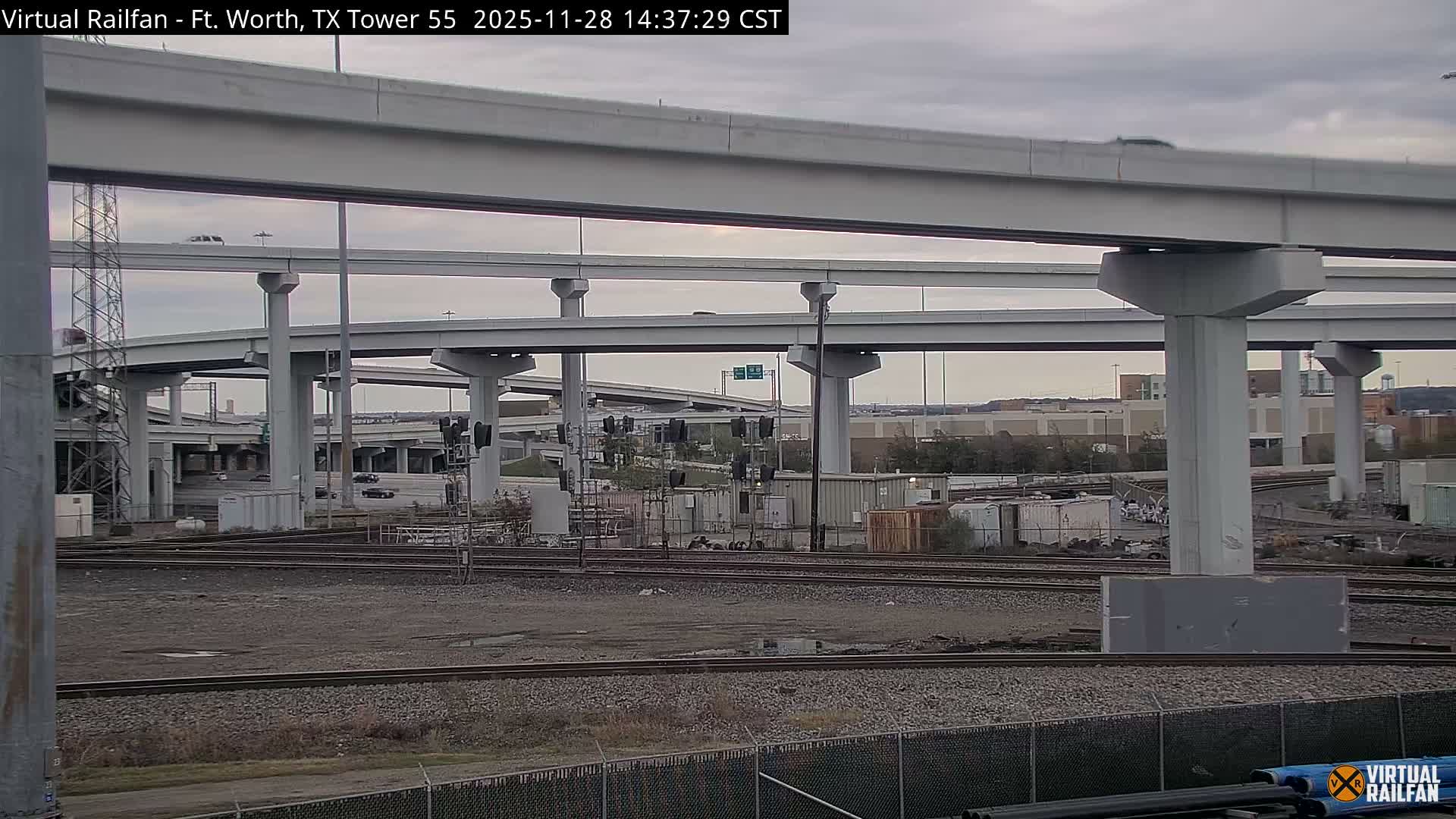 Multiple elevated concrete highway overpasses crisscross above a network of railroad tracks and industrial structures under a cloudy, overcast sky.