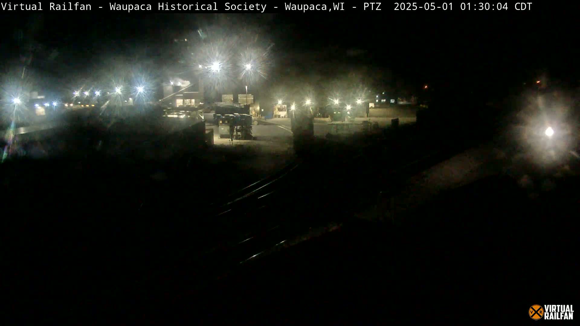 A nighttime, dimly lit industrial area is visible, with several buildings and some vehicles present under artificial lights.
