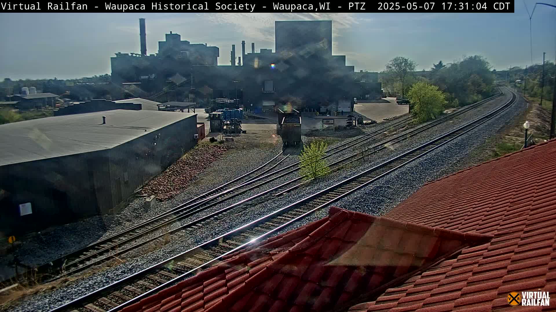 A sunny view of a rail yard with several train tracks leading toward a large industrial building.