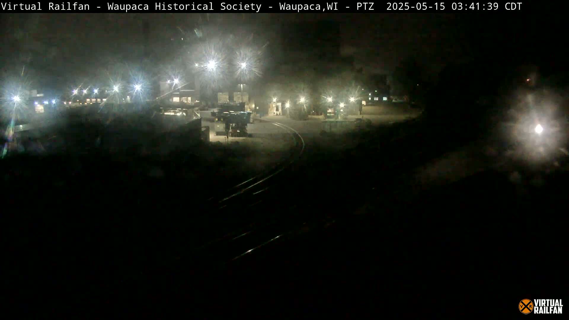 A nighttime view of a dimly lit rail yard with several pieces of equipment and tracks.