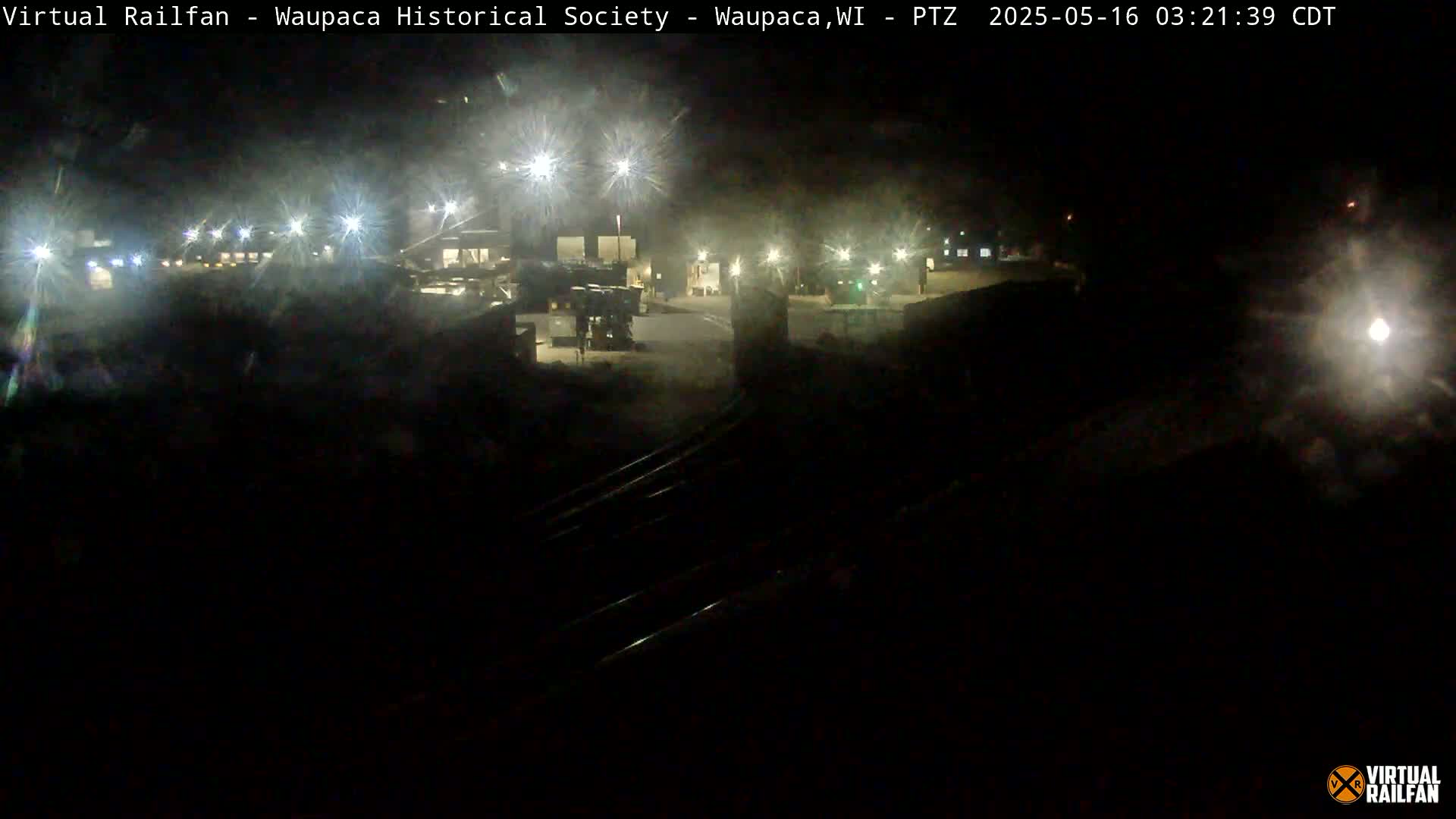 A nighttime view of a dimly lit industrial area with train tracks in the foreground.