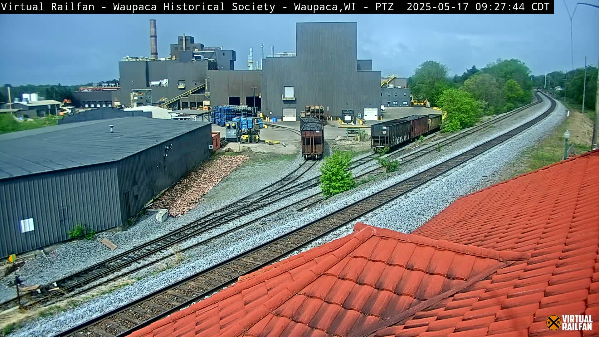 Railroad tracks converge near a large industrial building under a partly cloudy sky.