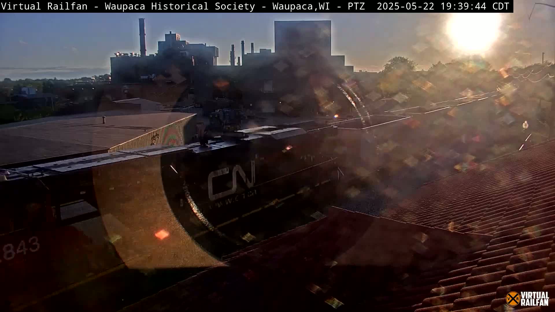 A CN train locomotive is visible at sunset, alongside industrial buildings and residential rooftops.