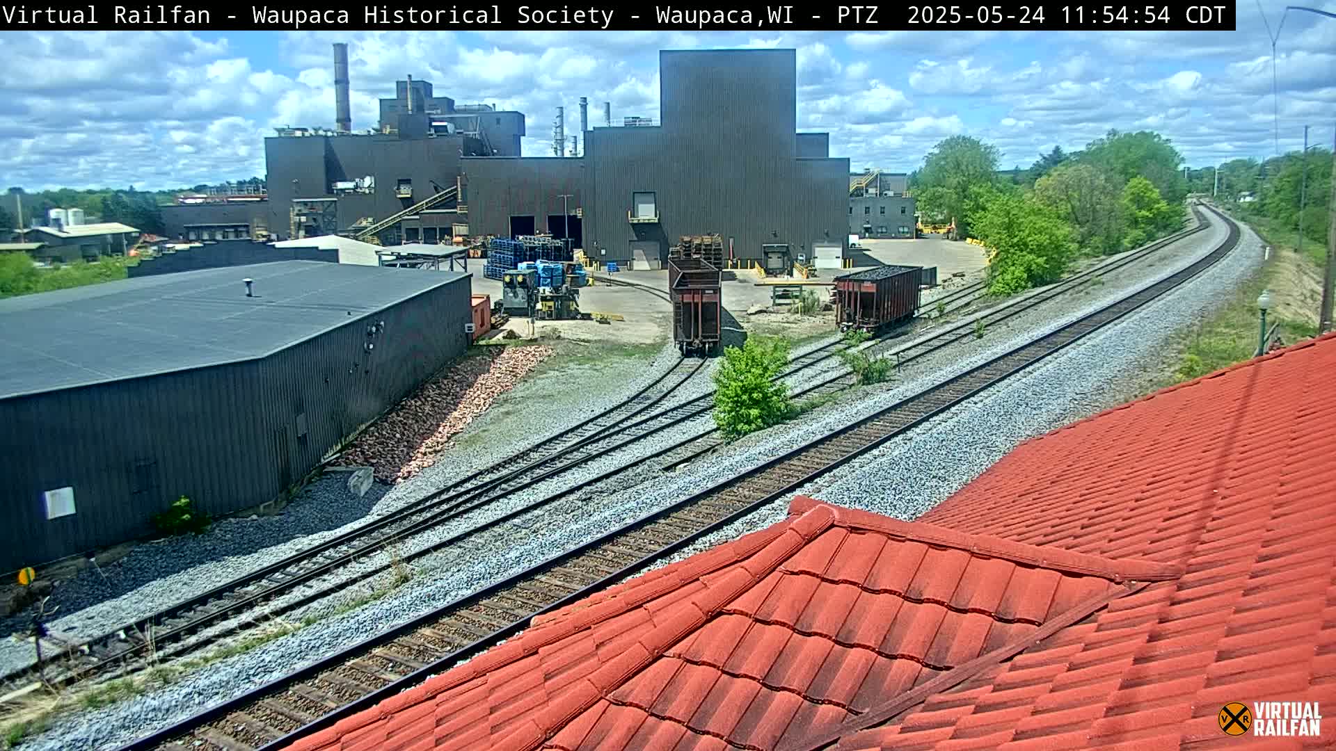A large industrial building is visible beyond railroad tracks that converge in the foreground, under a partly cloudy sky.