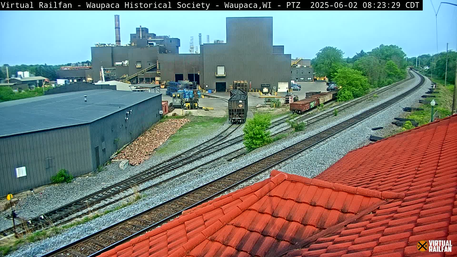 A train passes through a railway junction near an industrial complex on an overcast day.