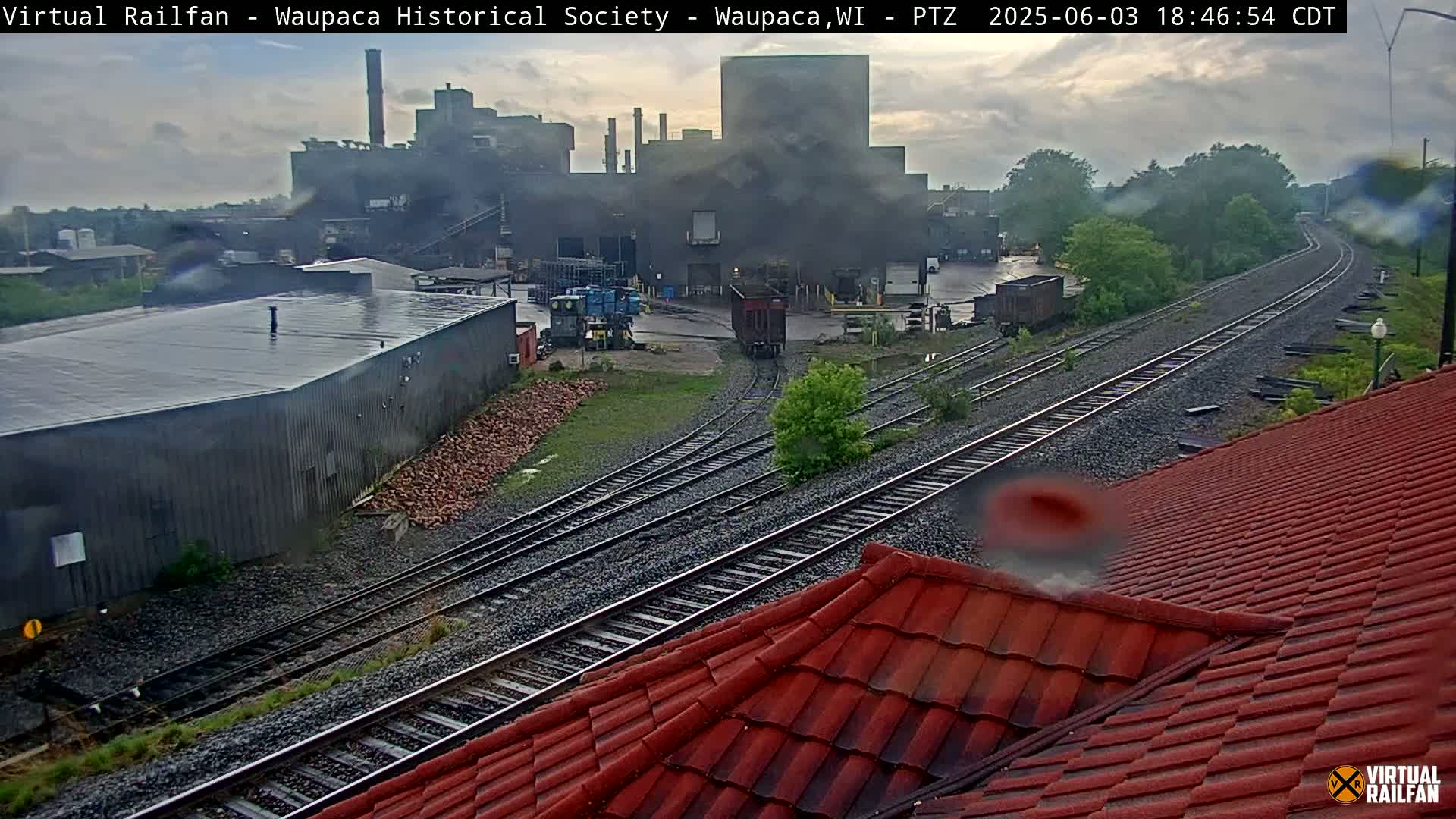 A view of railroad tracks curving past an industrial facility on a rainy day.