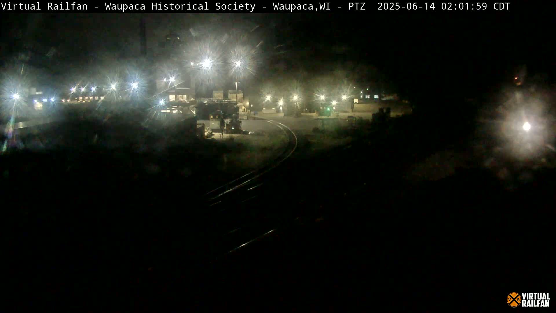 A nighttime view of a rail yard with several lights illuminating the area.