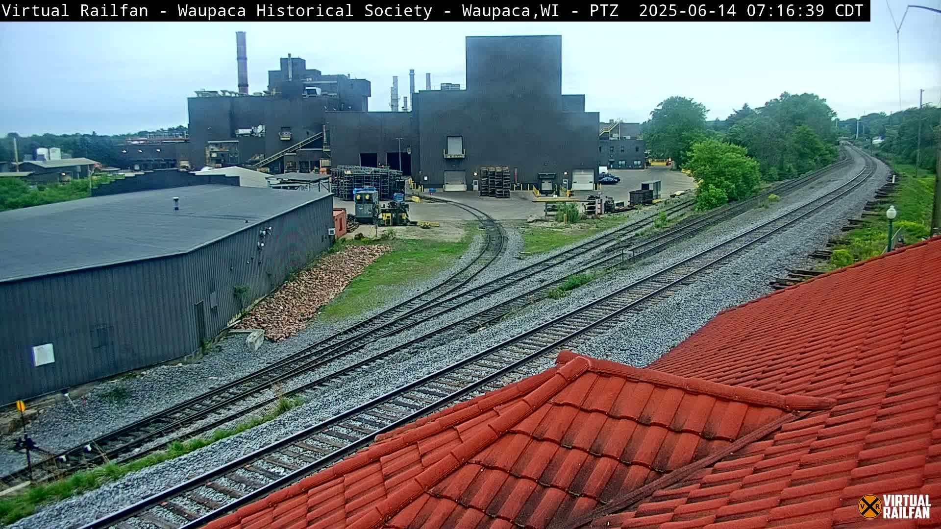 A large industrial building is situated beside a railway line on an overcast day.