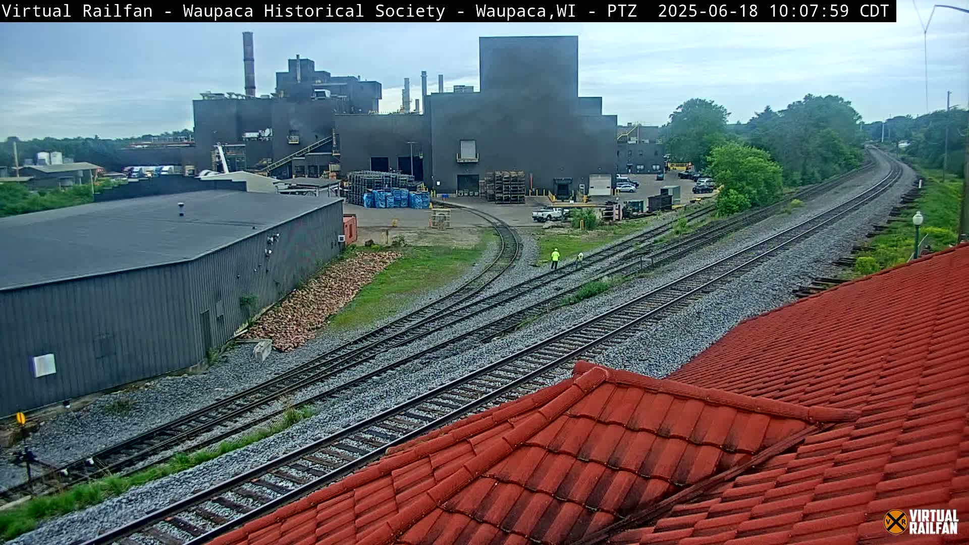 A large industrial building is visible next to railroad tracks under an overcast sky.