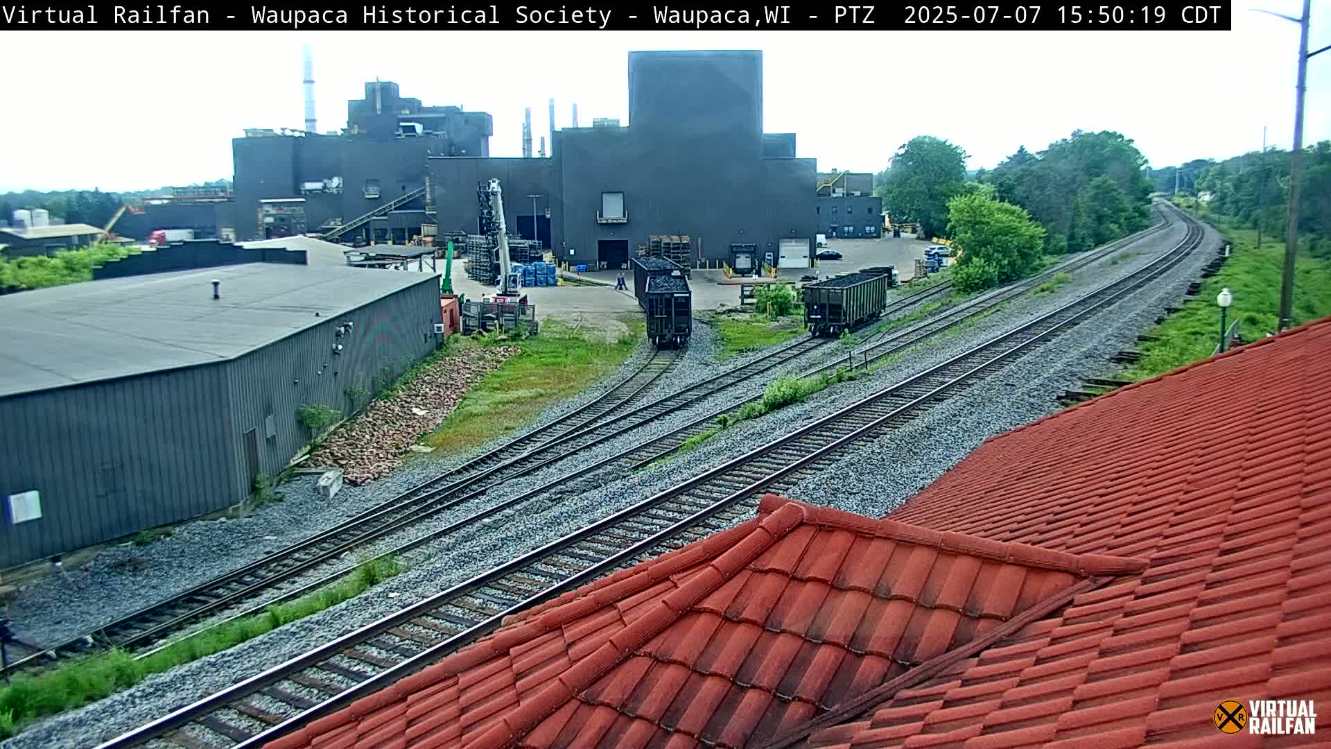 Two railway cars are visible on a track near a large industrial building on an overcast day.