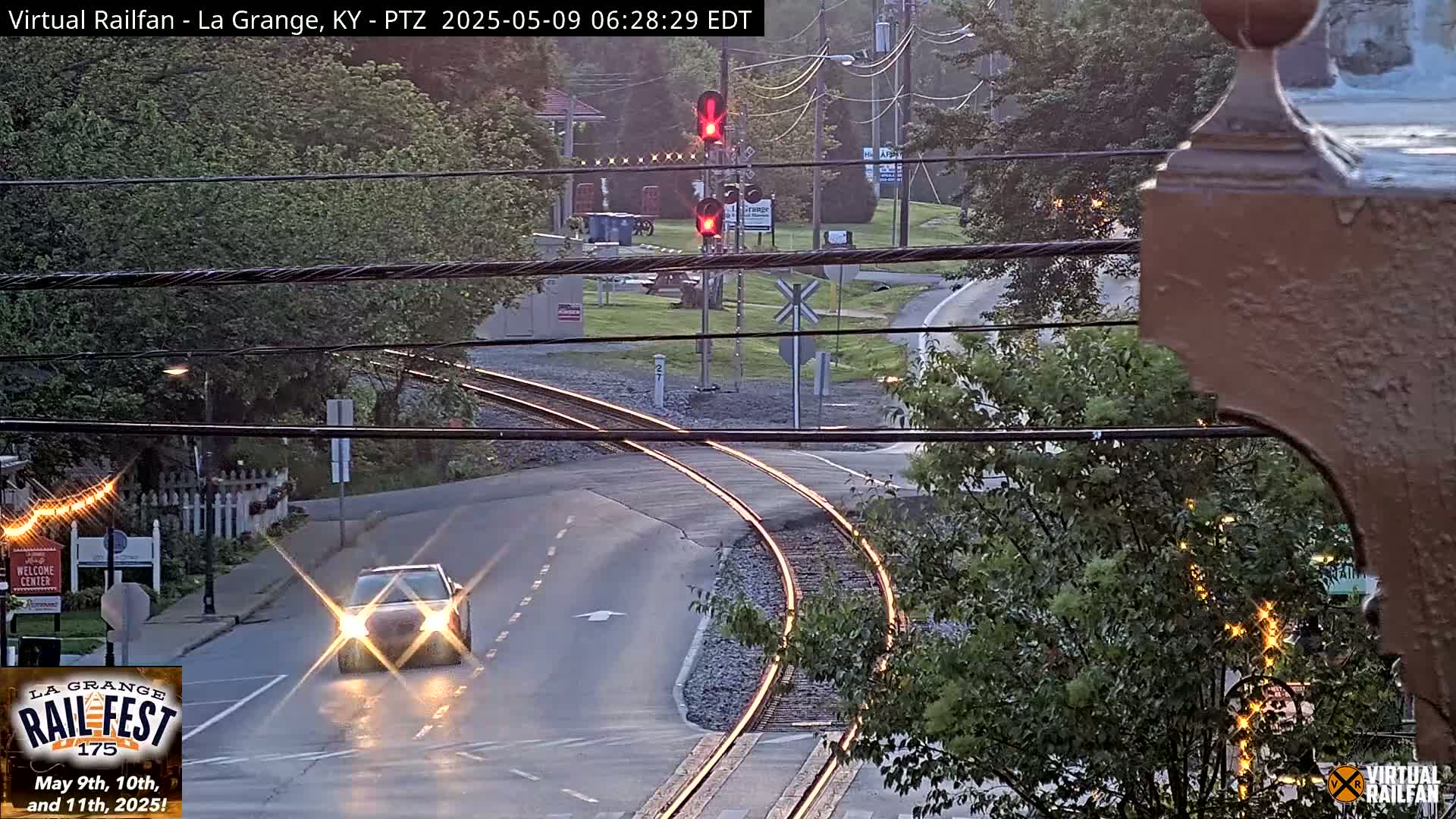 A car drives past a railroad crossing with a red traffic signal, under a twilight sky.