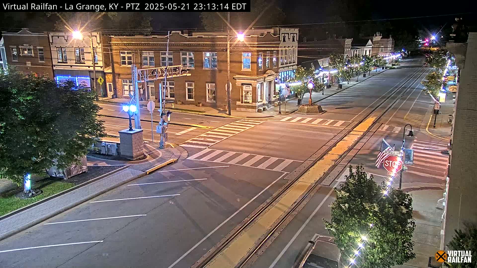A nighttime street scene shows a brick building and a mostly empty street with train tracks running down the middle, illuminated by streetlights.
