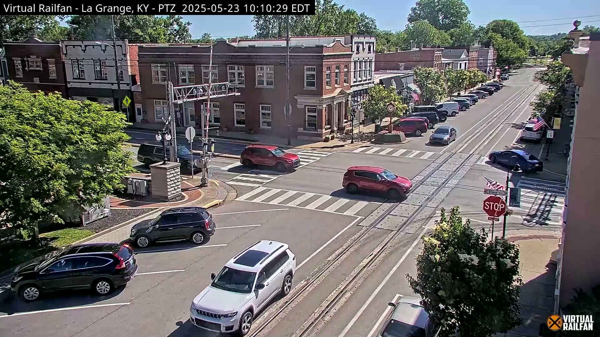 A sunny day in a small town, showing a street intersection with several cars and brick buildings.