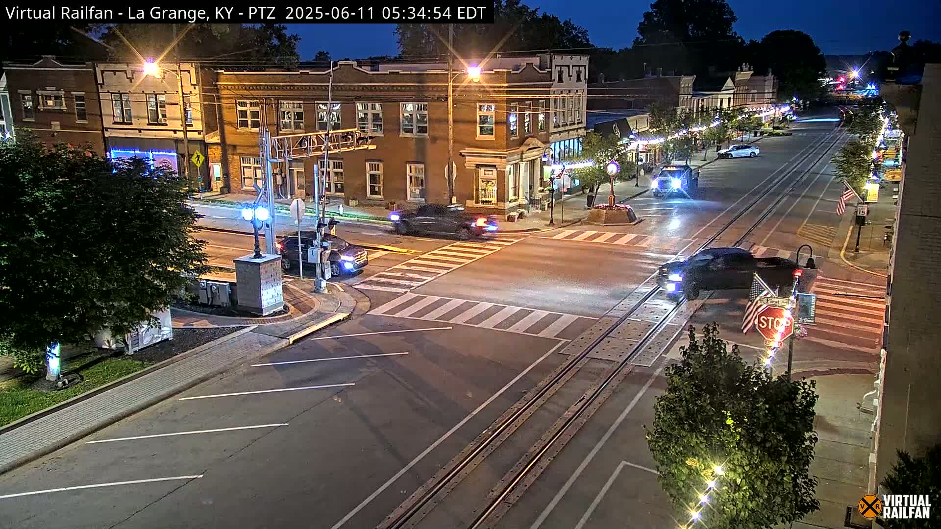 A nighttime street scene shows a town square with several vehicles at an intersection, under partly cloudy skies.