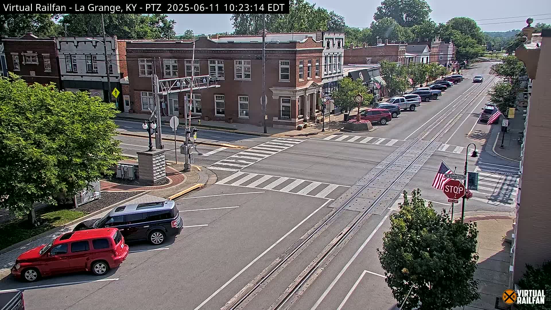 A sunny day reveals a small-town intersection with brick buildings, parked cars, and a streetcar track running down the middle of the road.